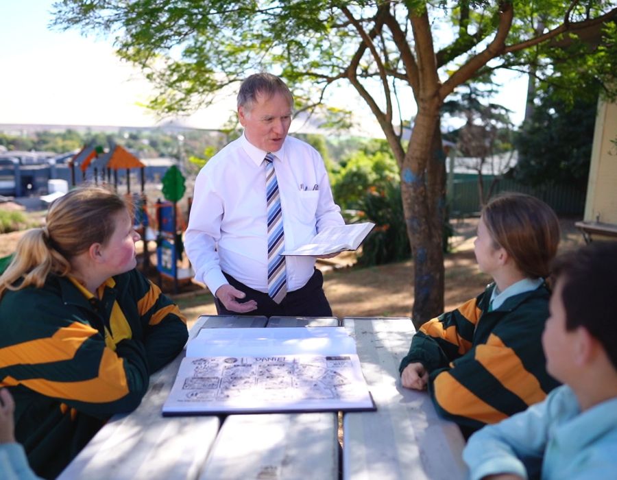 Teacher and students gathered around a table taking part in outdoor learning and spiritual growth
